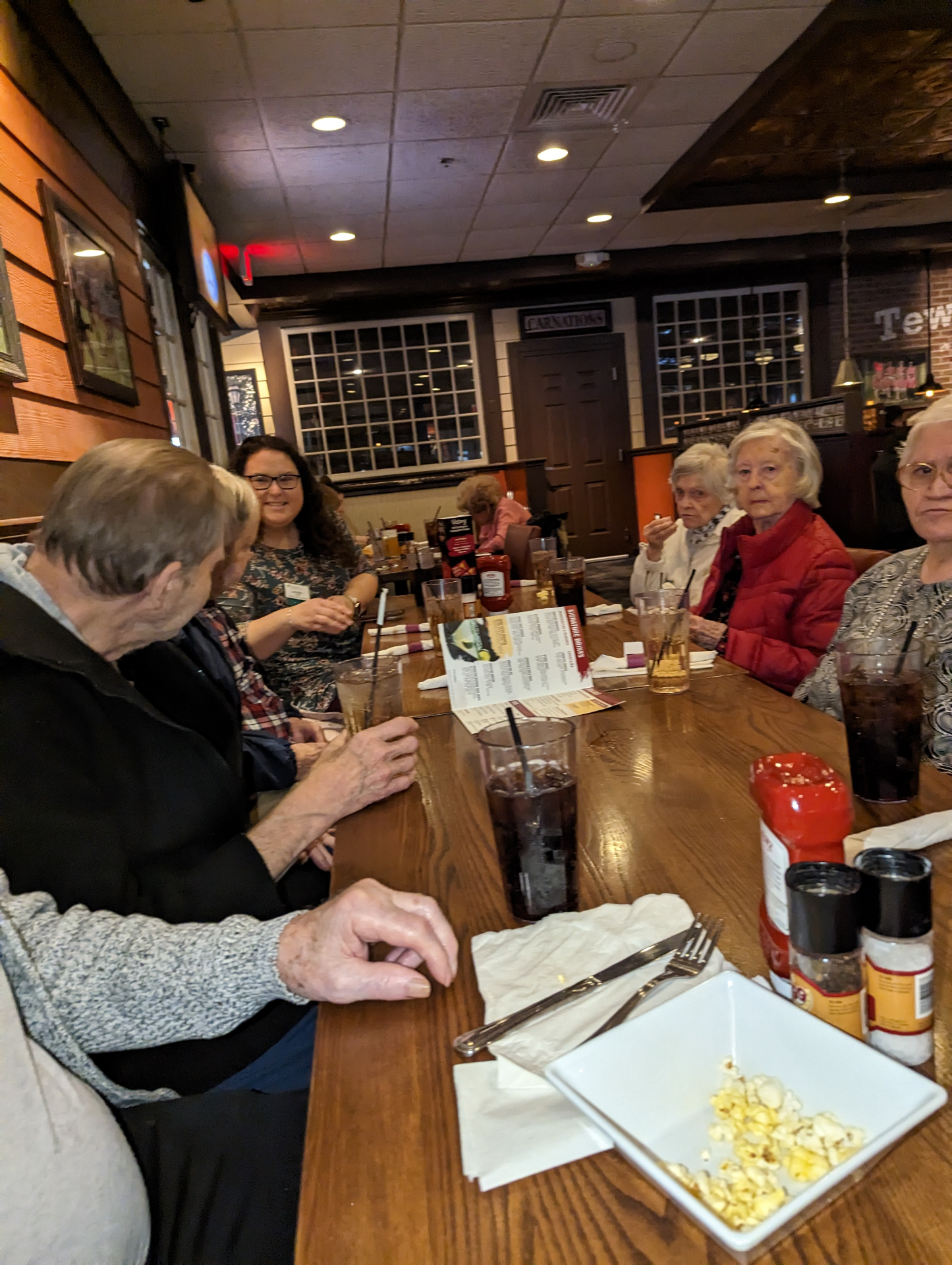 A caregiver sharing a meal at a restaurant with older clients around a wooden table.